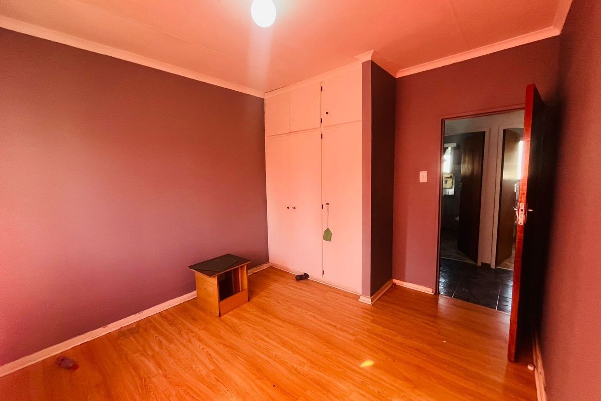 A bedroom featuring laminate flooring, built-in cupboards, and a doorway leading to an adjacent room.