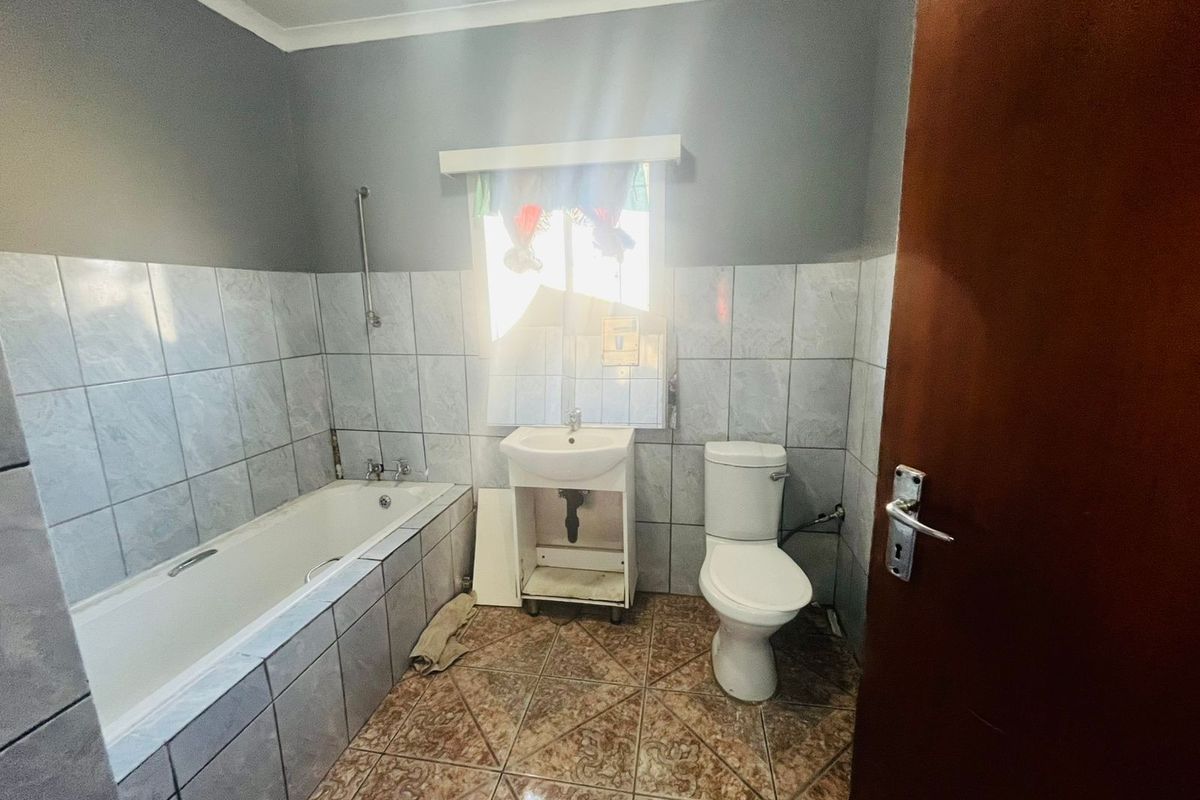 A functional bathroom featuring a built-in bathtub, pedestal-style sink, and toilet with tiled walls and flooring.