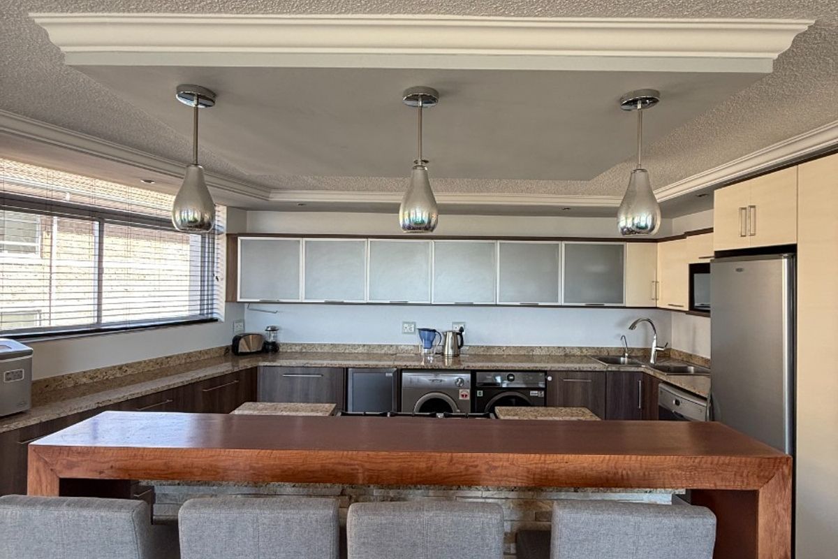A functional kitchen featuring a breakfast bar, stone countertops, integrated cabinetry, and a drop ceiling with pendant lighting.