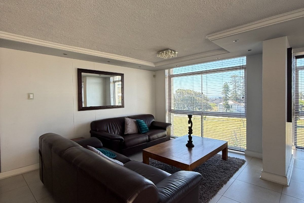 Spacious living area featuring large windows with natural light, tiled flooring, and decorative ceiling cornicing.