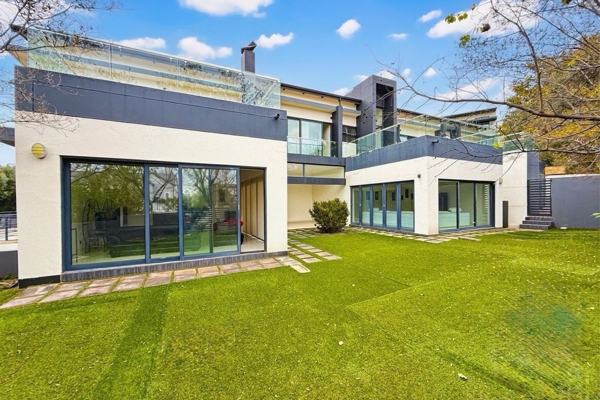 Modern rear exterior view of the property featuring large sliding glass doors, glass balustrades on the upper balconies, and a well-maintained lawn.