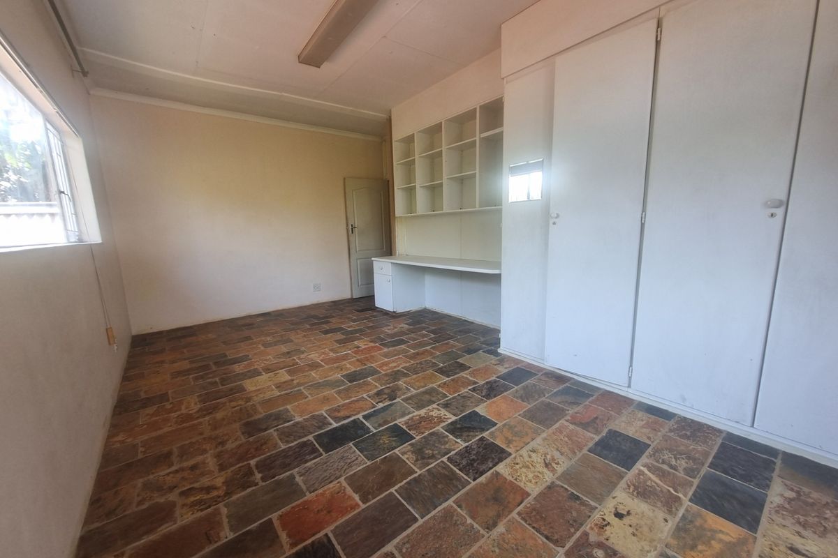 A bedroom featuring built-in storage, a desk area with shelving, and natural stone tile flooring.