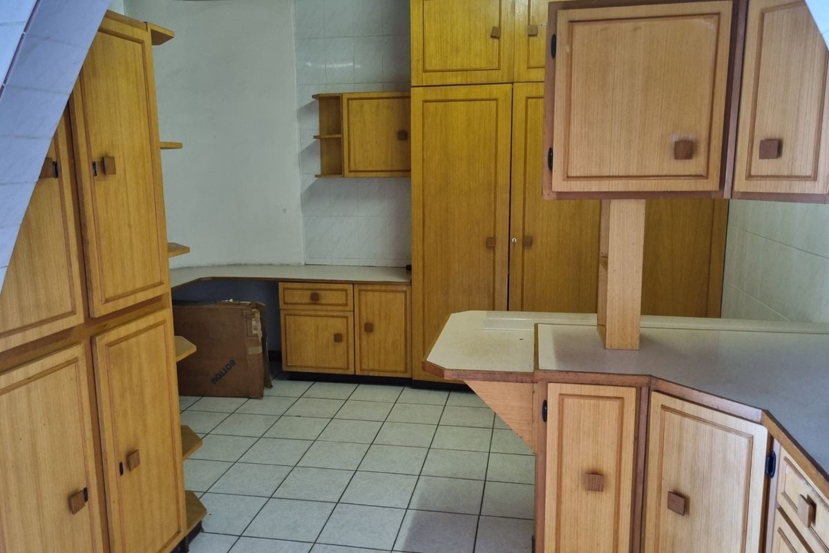 A dated kitchen featuring extensive wooden cabinetry, laminate countertops, and tiled flooring, offering a functional layout ready for modern renovation.