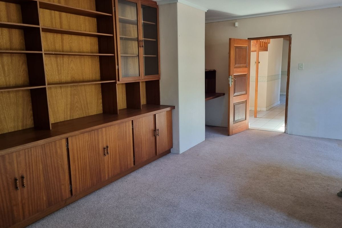 A spacious living area featuring built-in wooden shelving and cabinetry, with direct access to an adjoining hallway.