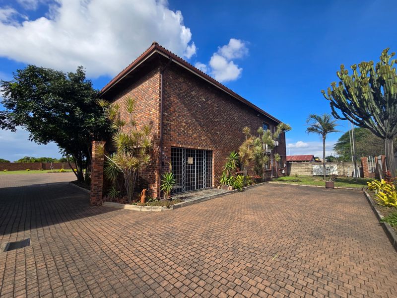 A view of the face brick office building exterior featuring a paved driveway and secure entrance gate.