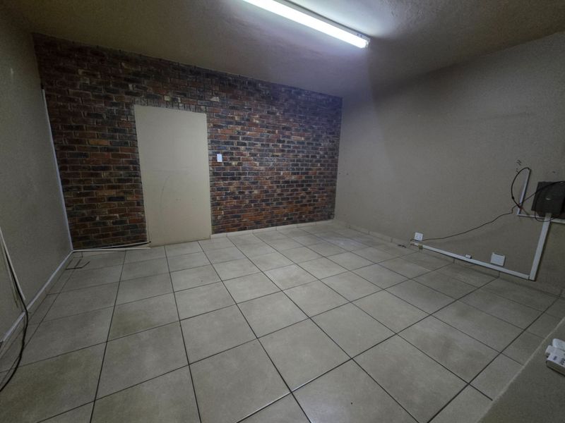 An empty office space featuring a rustic exposed brick wall, neutral tiled flooring, and functional overhead fluorescent lighting.