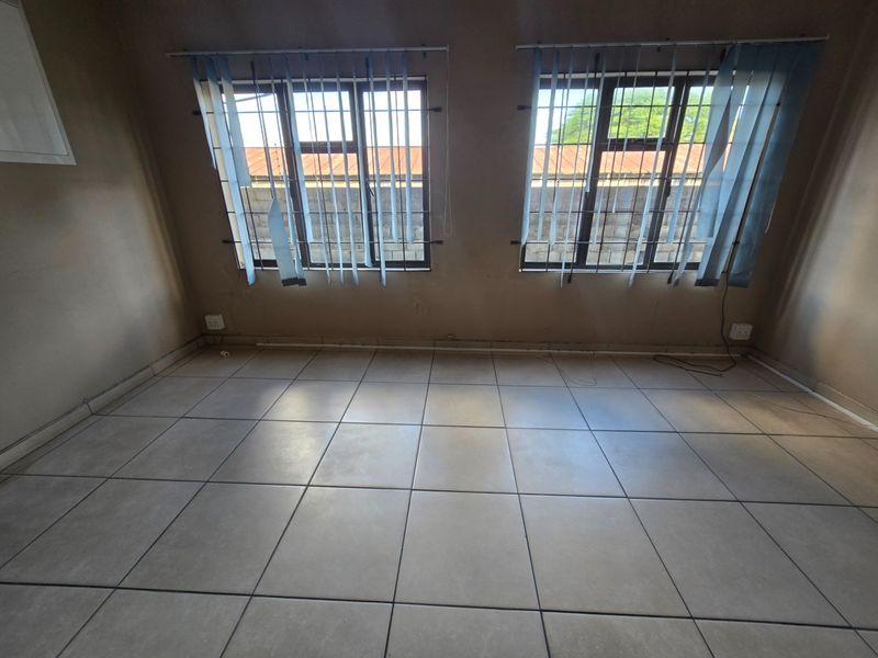 An empty office space featuring neutral floor tiles, security bars on windows, and vertical blinds, offering a blank canvas for professional use.