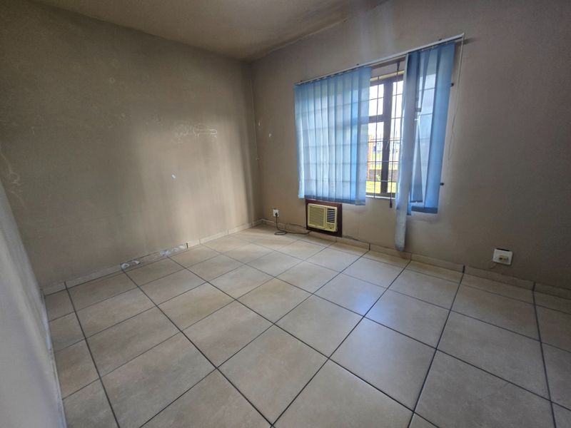 An empty office space featuring ceramic tiled flooring, a built-in air conditioning unit, and window security bars with vertical blinds.