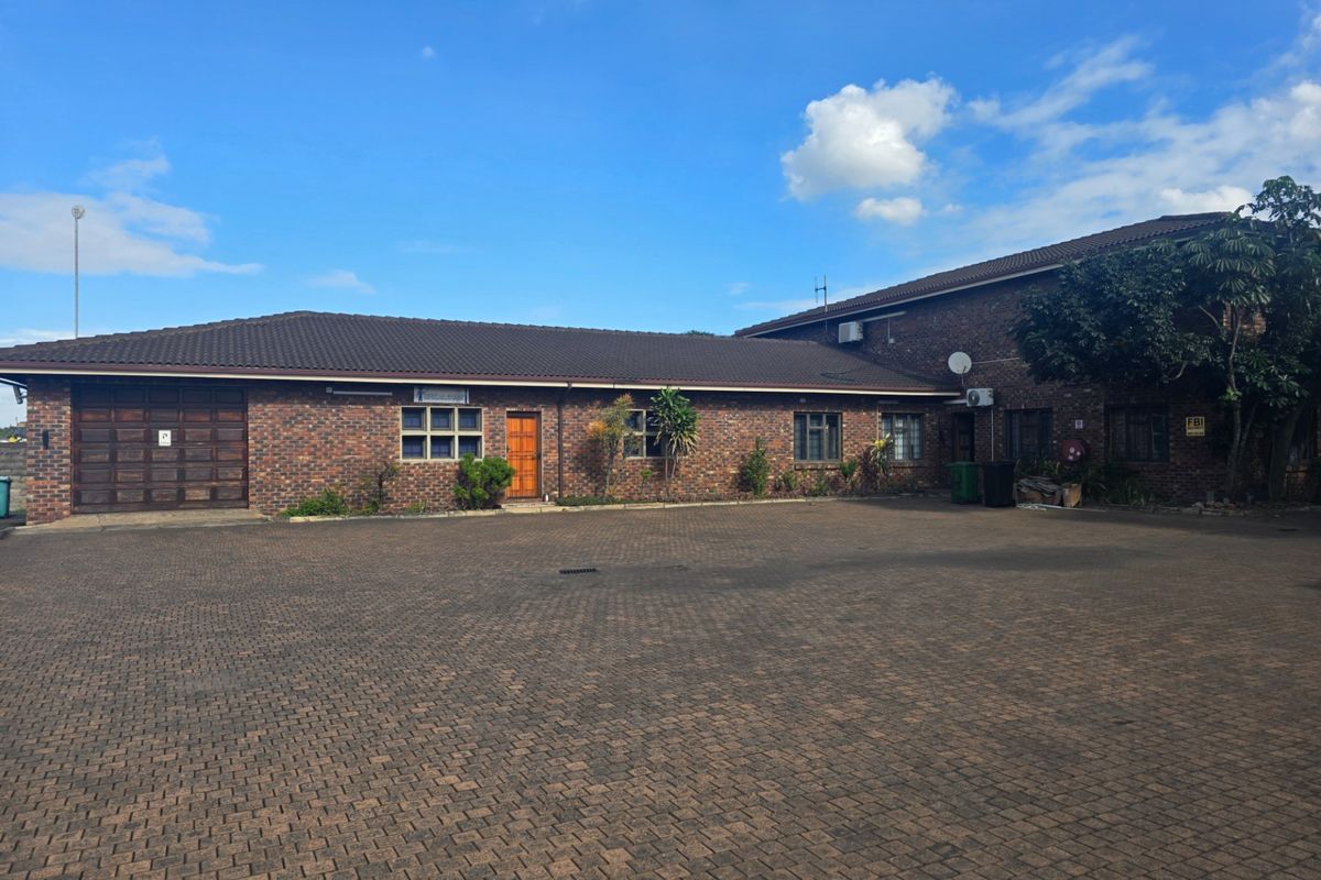 Front exterior view of a brick office building featuring a large paved parking area, garage access, and multiple window openings.