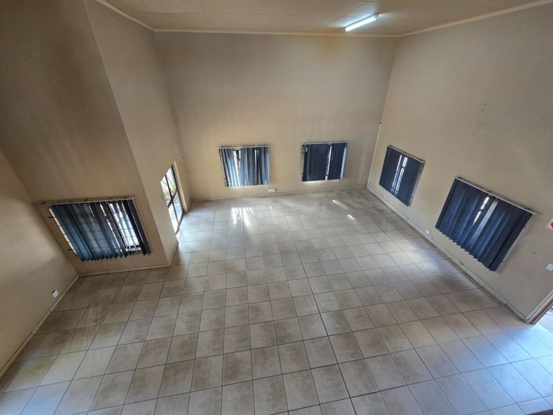 A spacious, empty office area featuring tiled flooring, multiple windows with vertical blinds, and overhead fluorescent lighting.
