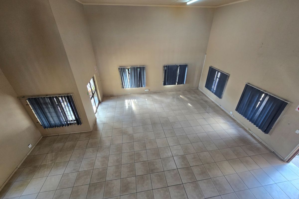 A spacious, empty office area featuring tiled flooring, multiple windows with vertical blinds, and overhead fluorescent lighting.