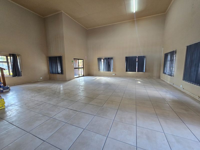 A spacious, empty office area featuring neutral walls, tiled flooring, and multiple windows with vertical blinds, offering a versatile workspace.