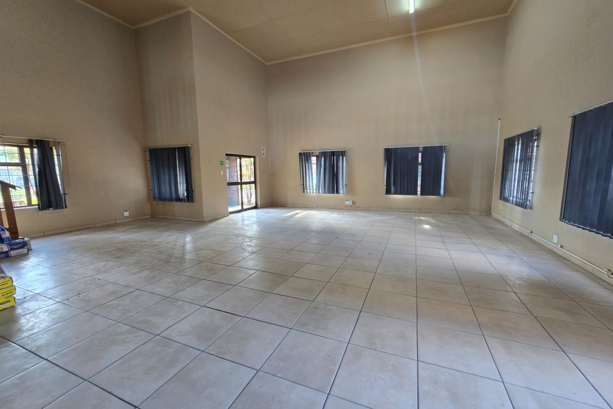 A spacious, empty office area featuring neutral walls, tiled flooring, and multiple windows with vertical blinds, offering a versatile workspace.