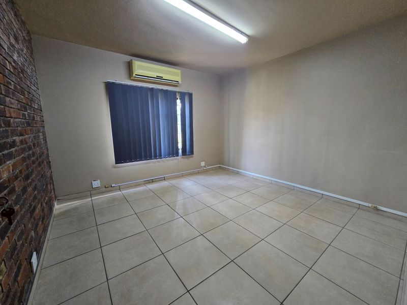 An empty office space featuring ceramic floor tiles, an exposed brick feature wall, and a wall-mounted air conditioning unit.