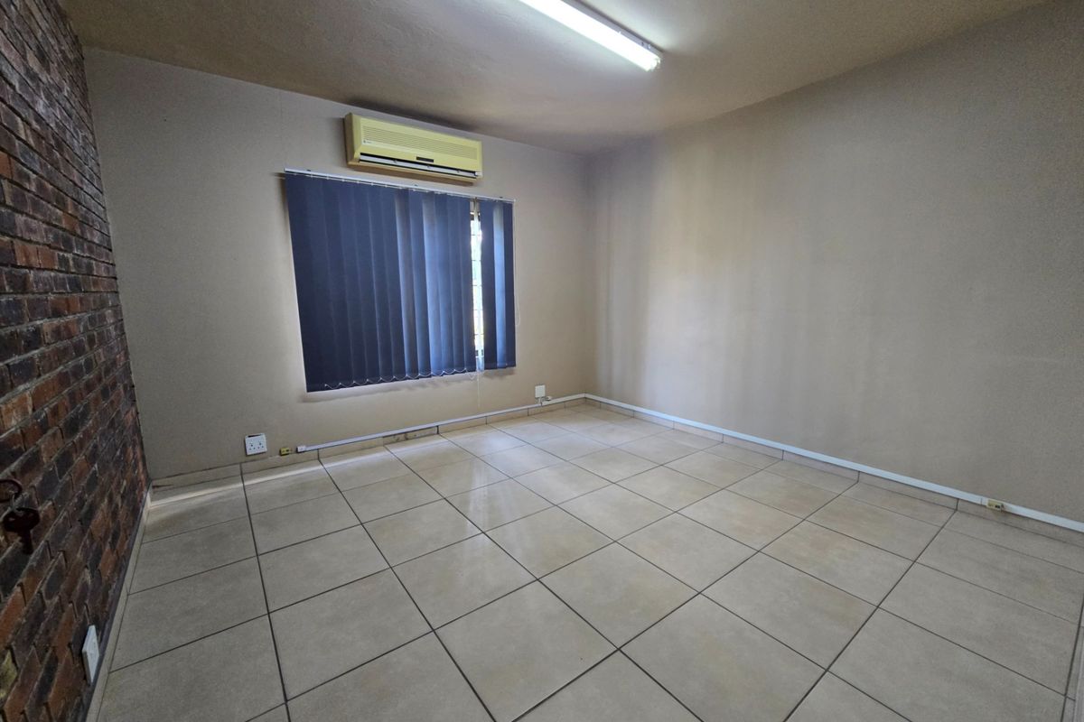 An empty office space featuring ceramic floor tiles, an exposed brick feature wall, and a wall-mounted air conditioning unit.