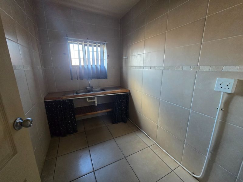 A functional laundry area featuring tiled walls and flooring, a stainless steel sink, and a window with security bars.