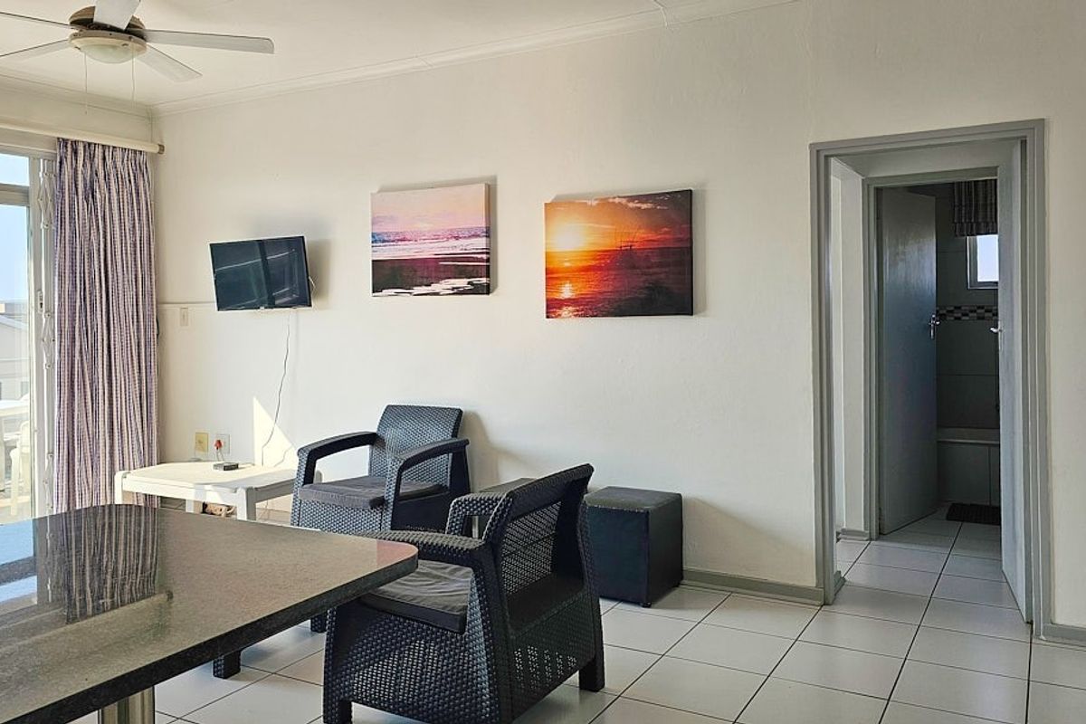 A living area featuring white tiled flooring, a ceiling fan, and direct access to an outdoor balcony through a sliding glass door.