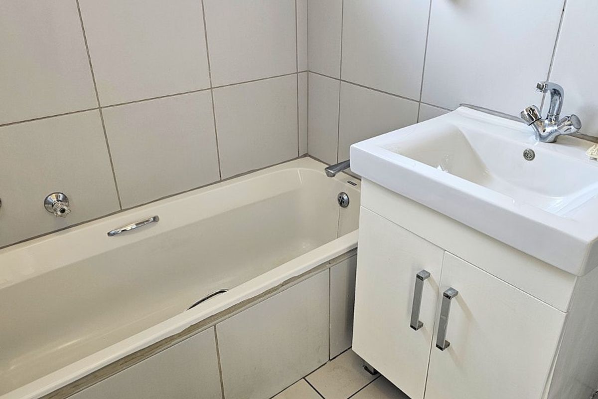 A functional bathroom featuring a built-in bathtub with wall-mounted taps and a vanity unit with a basin.