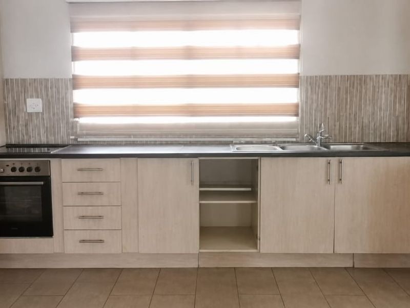 A functional kitchen featuring light wood-finish cabinetry, a built-in oven, electric hob, and a double sink with a tiled backsplash.