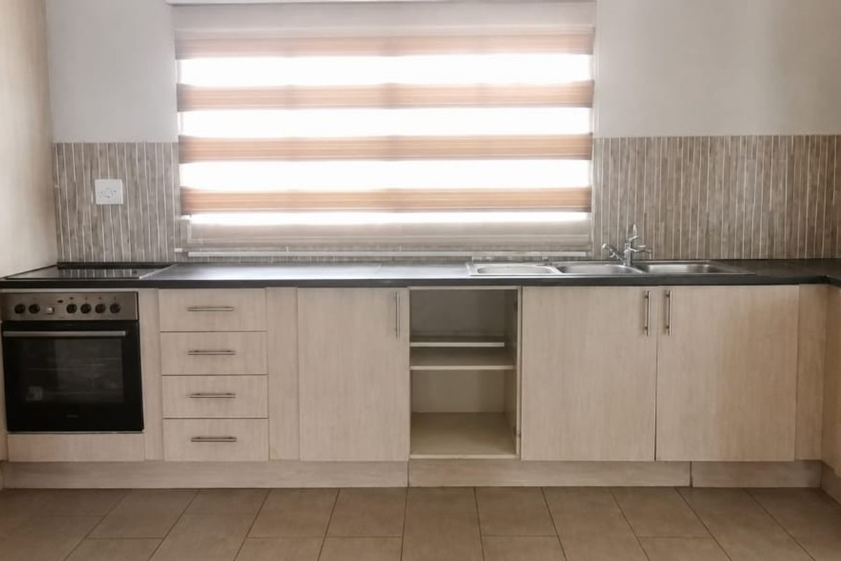 A functional kitchen featuring light wood-finish cabinetry, a built-in oven, electric hob, and a double sink with a tiled backsplash.