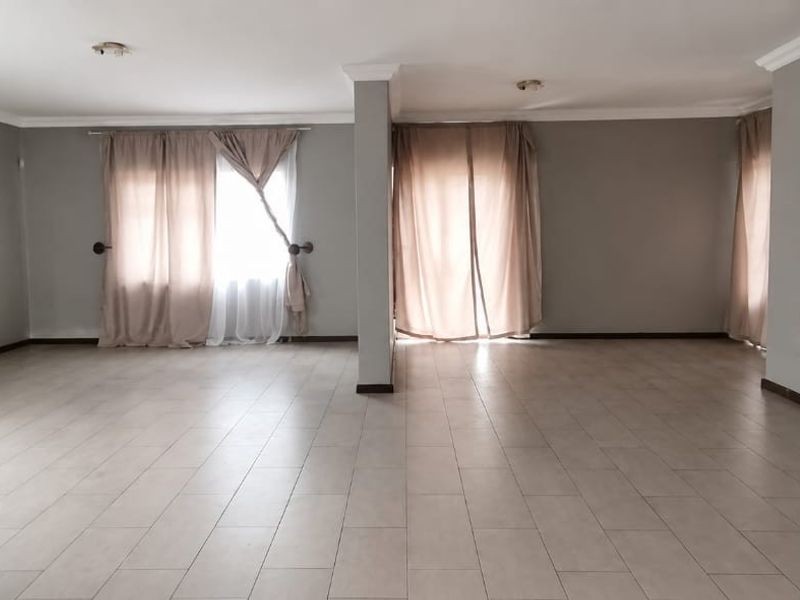 A spacious, open-plan living area featuring neutral tiled flooring, crown molding, and large windows with curtains, offering a bright and versatile blank canvas.
