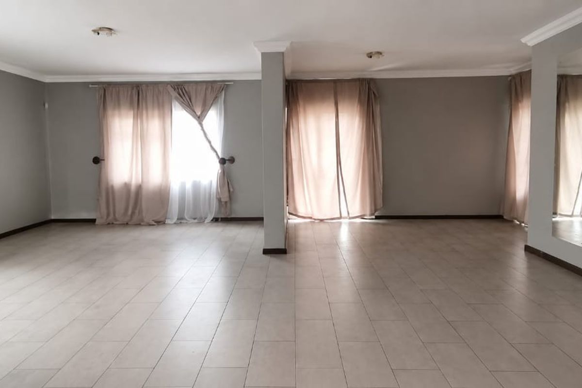 A spacious, open-plan living area featuring neutral tiled flooring, crown molding, and large windows with curtains, offering a bright and versatile blank canvas.