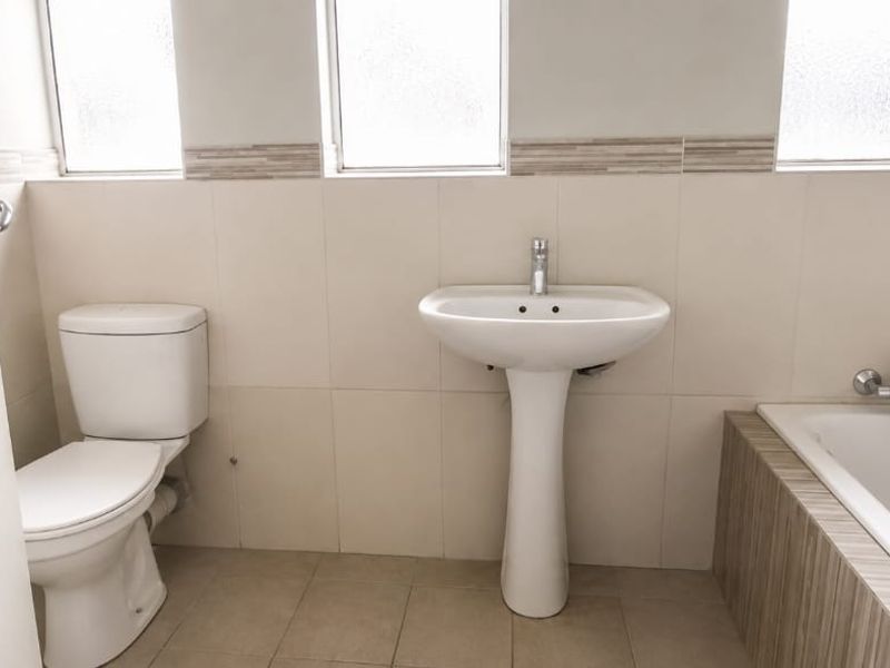 A clean, functional bathroom featuring a pedestal basin, toilet, and bathtub with neutral wall and floor tiling.