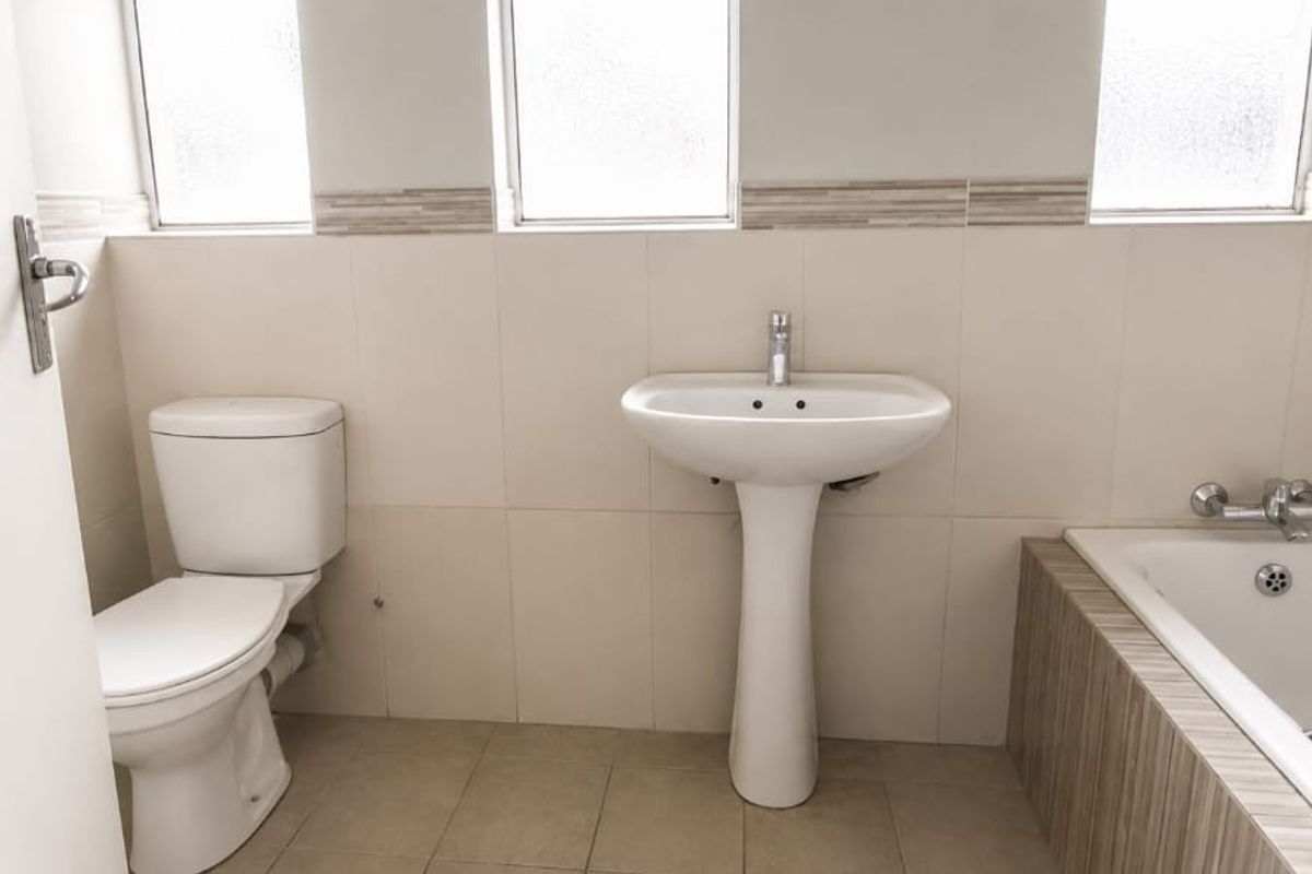A clean, functional bathroom featuring a pedestal basin, toilet, and bathtub with neutral wall and floor tiling.
