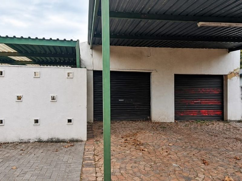 A double garage with roller shutter doors and an attached carport, featuring a paved driveway and perimeter boundary walling.