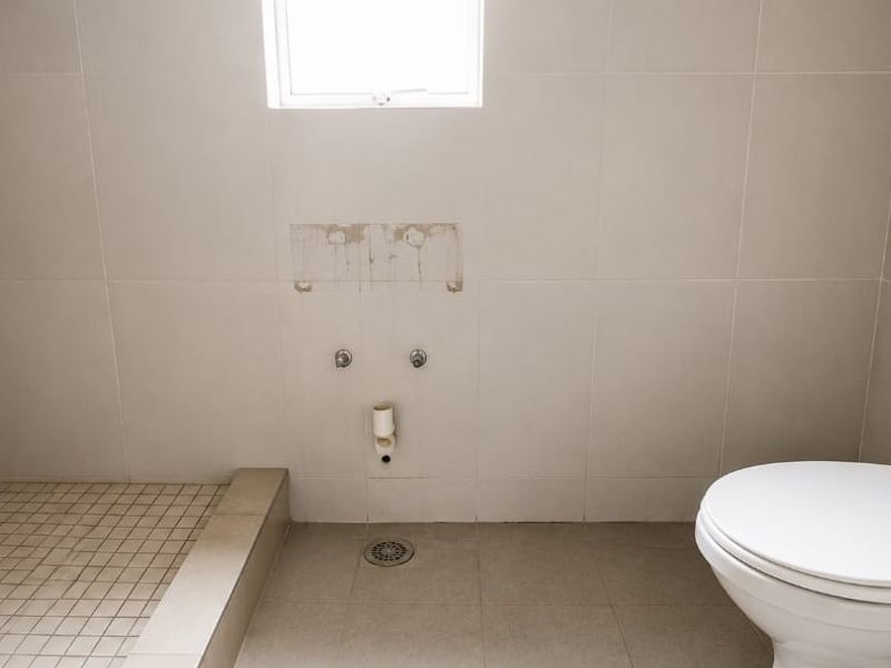 A partially finished bathroom featuring a toilet and tiled shower area, currently missing a vanity and sink fixtures.