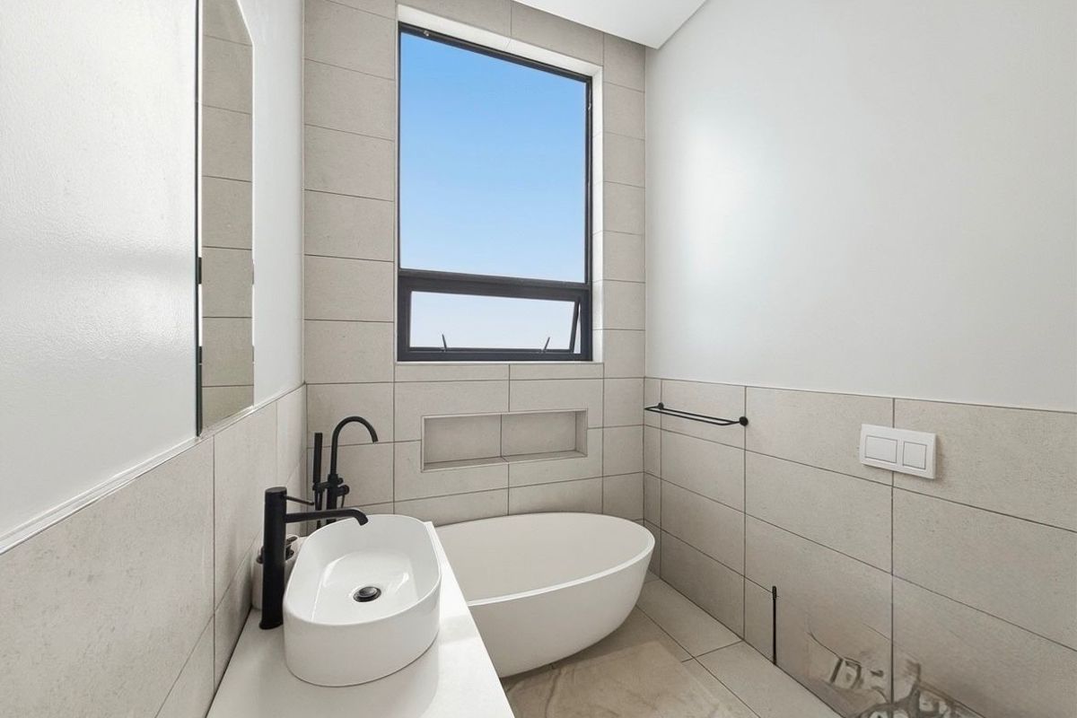 Modern bathroom featuring a freestanding bathtub, vessel sink with matte black fixtures, and neutral wall tiling.