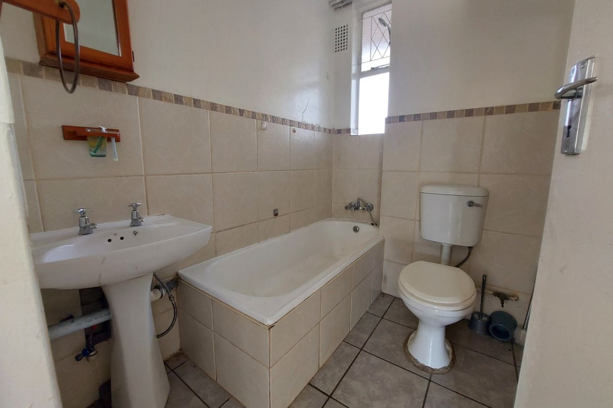 A dated bathroom featuring a pedestal basin, standard bathtub, and toilet with neutral wall tiling and tiled flooring.