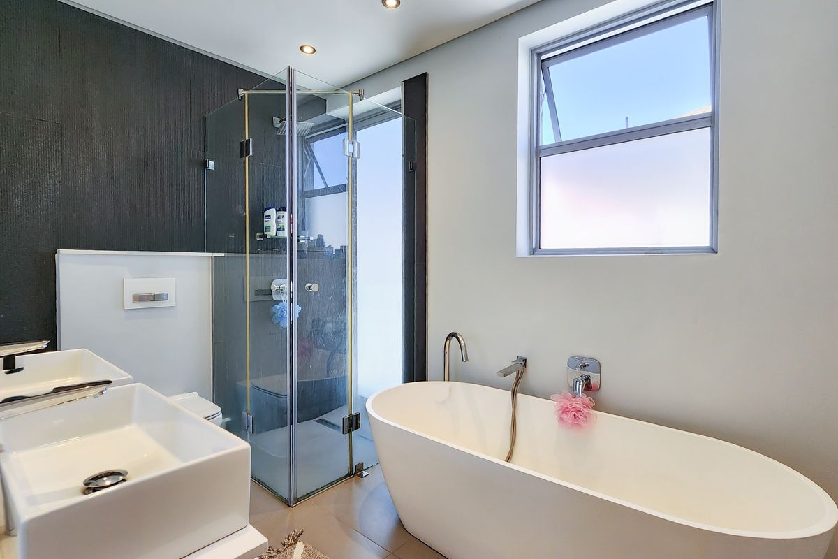Modern bathroom featuring a sleek freestanding bathtub, glass-enclosed shower, and dual vanity basins with contemporary wall-mounted fixtures.