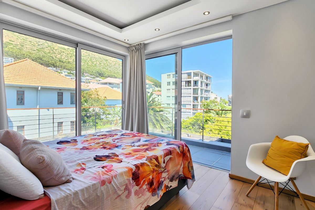 Modern bedroom featuring hardwood flooring, a tray ceiling with recessed lighting, and large sliding glass doors opening onto a private balcony with scenic views.