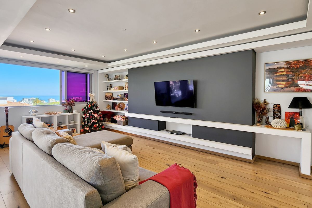 A modern living room featuring hardwood flooring, recessed lighting, and a sleek, custom-built media wall with integrated shelving and cabinetry.