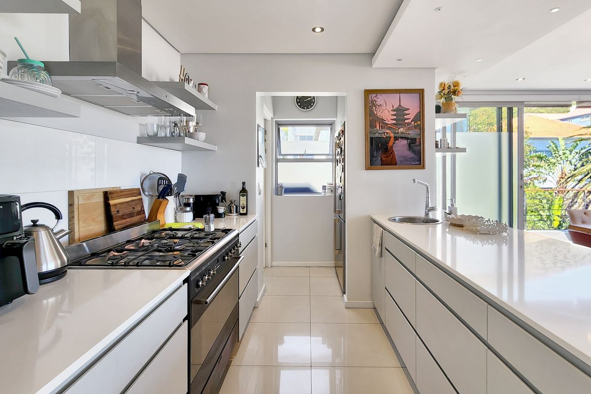 Modern kitchen featuring sleek white cabinetry, quartz countertops, a gas hob, stainless steel extractor, and polished porcelain floor tiles with integrated downlighting.