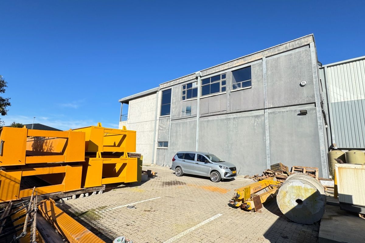 Rear exterior view of an industrial building featuring concrete panel construction, large windows, and an adjacent paved yard area.