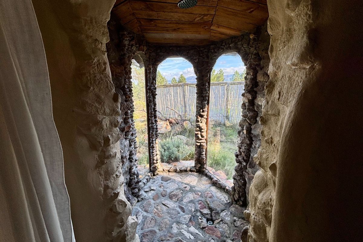 A unique rustic outdoor-style shower featuring natural stone masonry, arched openings, and a wooden ceiling, offering scenic views of the surrounding landscape.