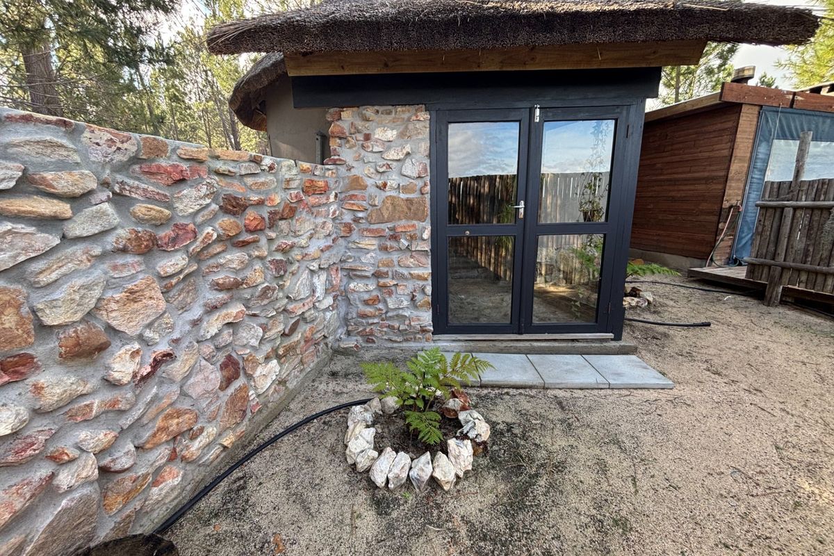 A charming exterior view of a rustic stone-walled structure with a thatched roof and dark-framed glass double doors.