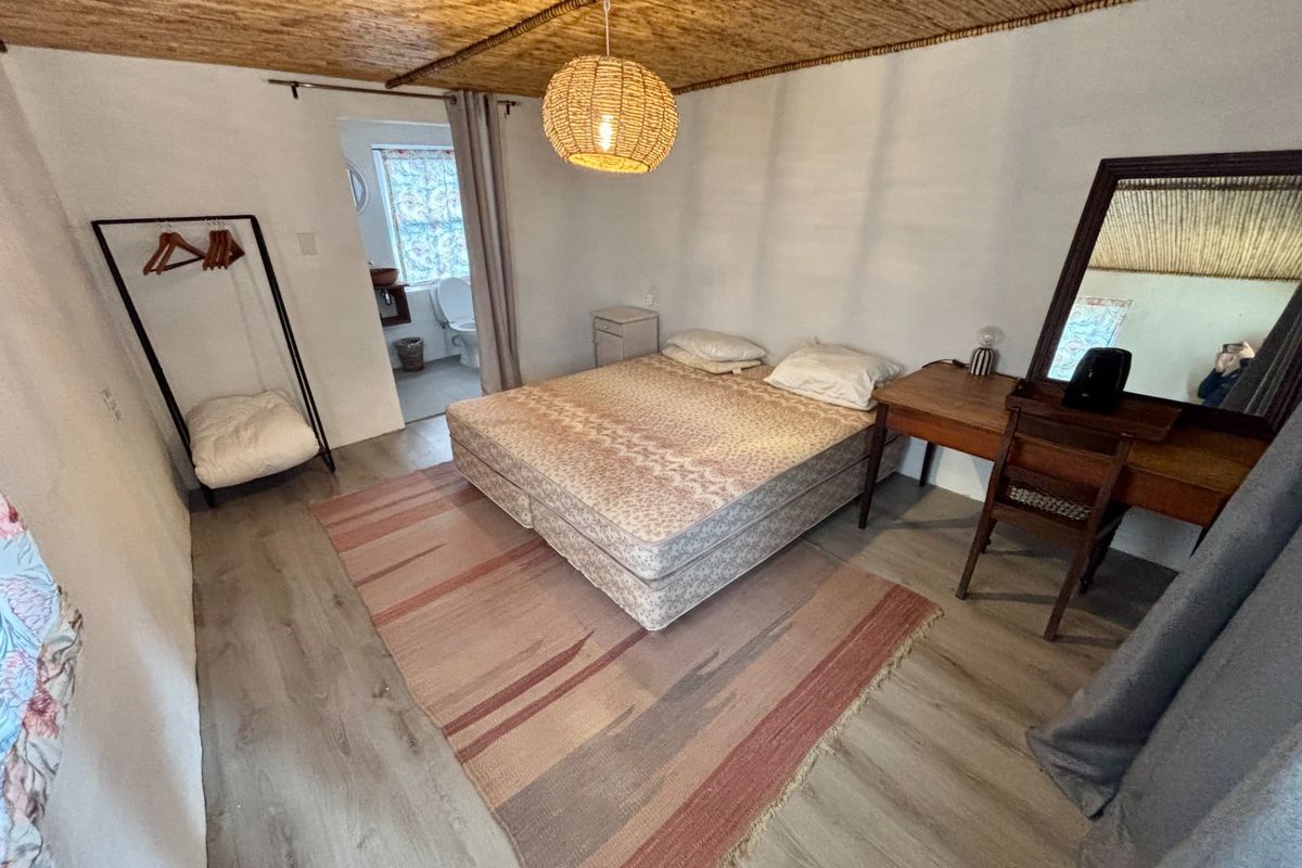 A rustic bedroom featuring a unique thatched ceiling, wood-look flooring, and an en-suite bathroom access.