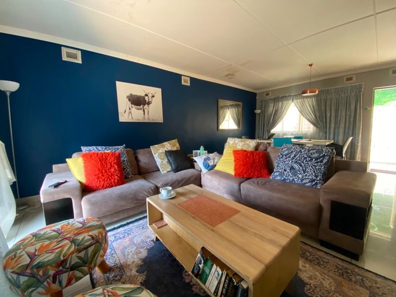 A spacious living room featuring a bold blue accent wall, tiled flooring, and large windows with curtains, providing a comfortable and functional living space.