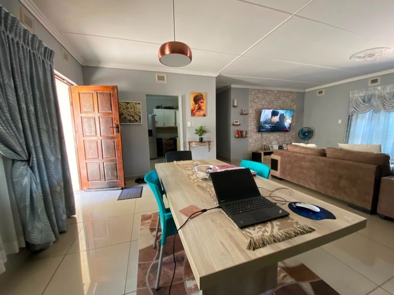 Open plan living and dining area featuring tiled flooring, a stone-cladding feature wall, and direct access to the kitchen and exterior entrance.