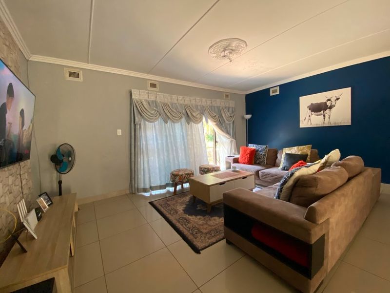 A comfortable living room featuring tiled flooring, a decorative ceiling rose, and a bold blue accent wall, providing a functional and inviting space.