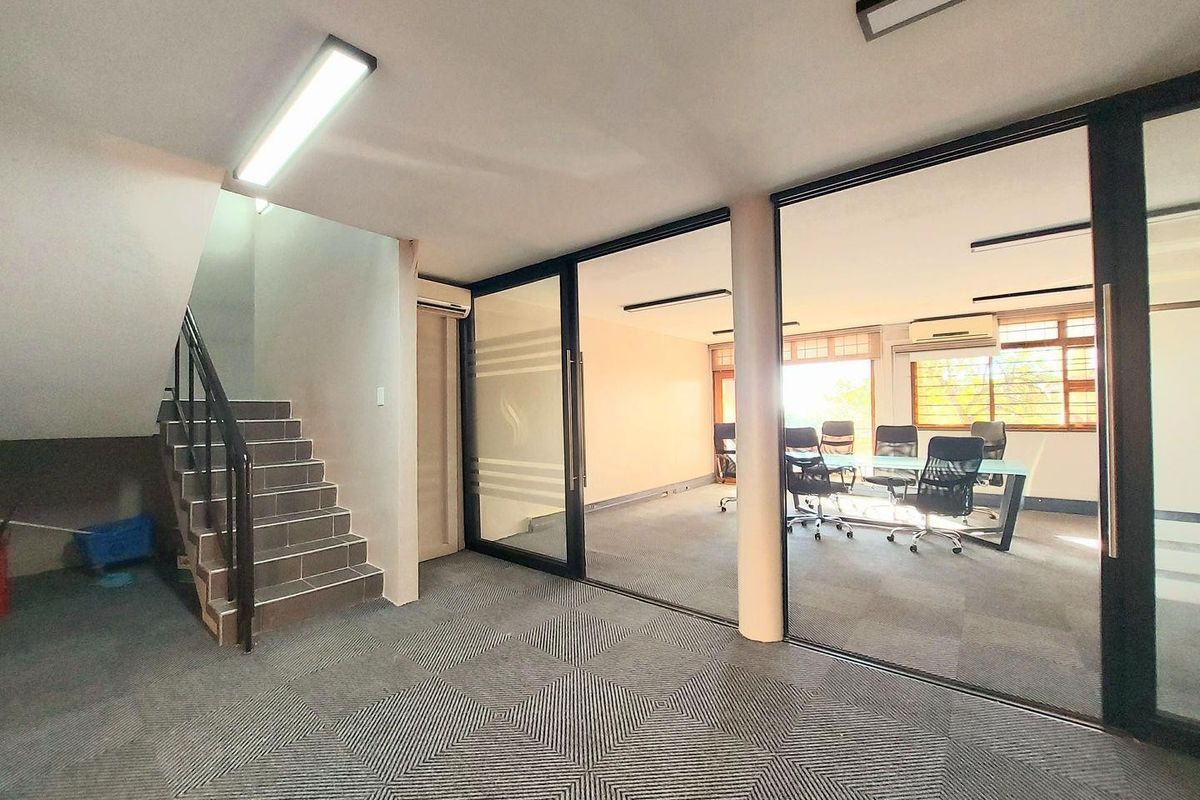 Commercial office space featuring a staircase, glass-partitioned meeting room, carpeted flooring, and integrated air conditioning units.