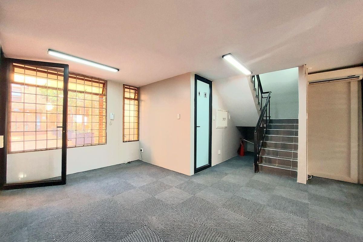 Commercial office space featuring patterned carpeting, integrated fluorescent lighting, a private restroom, and an internal staircase leading to upper levels.