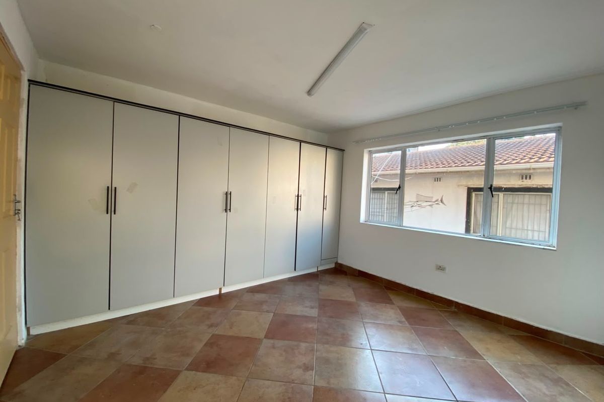 A bedroom featuring built-in floor-to-ceiling cabinetry, tiled flooring, and a large window providing natural light.
