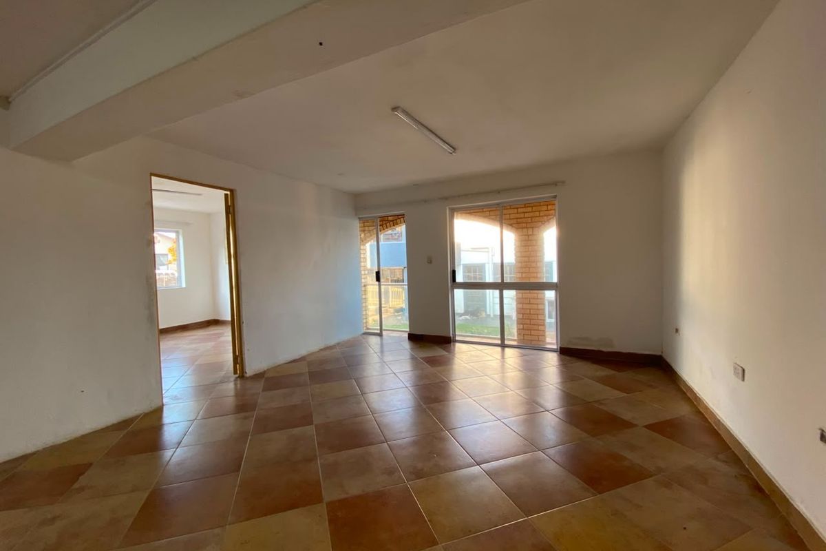 An empty living area featuring tiled flooring, large sliding glass doors providing natural light, and direct access to an adjacent room.