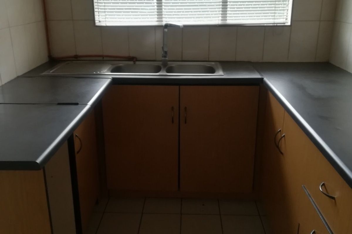 A functional kitchen featuring U-shaped laminate countertops, double stainless steel sink, tiled splashbacks, and built-in wooden cabinetry with ample storage space.