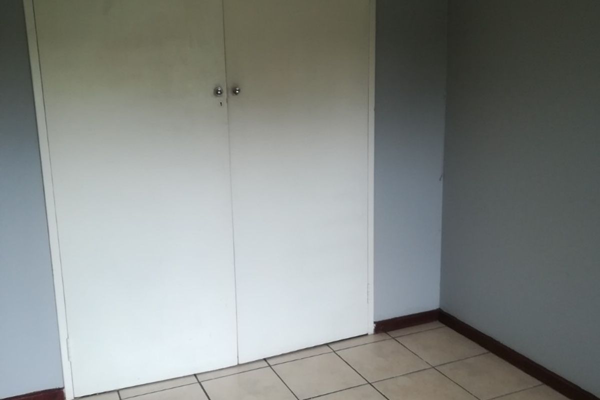 A simple bedroom featuring neutral tiled flooring and built-in storage cupboards with overhead cabinets.