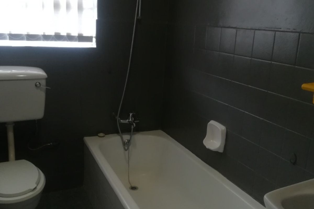 A functional bathroom featuring a bathtub with a handheld shower attachment, a standard toilet, and dark wall tiling.